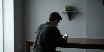 Pessoa de costas, hunched sobre um smartphone com tela verde brilhante, em um ambiente minimalista e moderno, simbolizando o impacto neurocognitivo da hiperconectividade. O ambiente possui uma planta suculenta verde, e a luz dramática enfatiza a imersão na tecnologia.